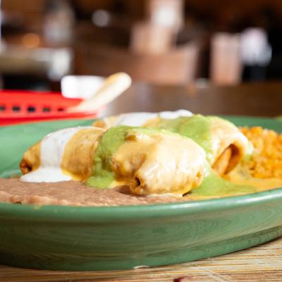 A close-up of chimichangas with guacamole, sour cream, rice, and refried beans.