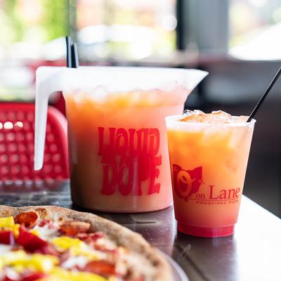 A pitcher and a glass of orange iced drink with a pizza in the foreground.
