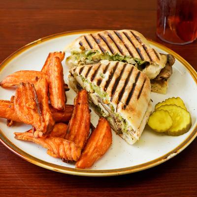 Chicken Pesto Avocado Ciabatta sandwich, served with sweet potato fries and pickles.