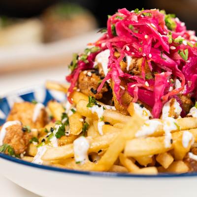 Fries with tomato sauce, yogurt sauce, pickled red cabbage, paprika chili oil, and sesame seeds.