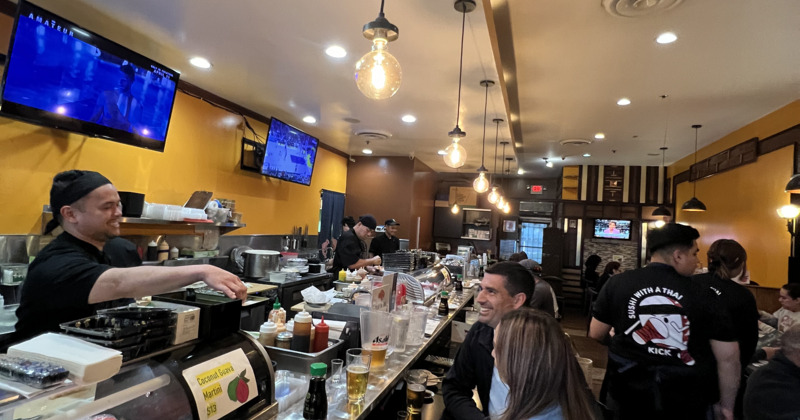 A vibrant restaurant scene featuring people sitting at the counter and staff in action