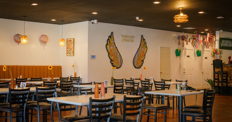 Casual dining area with tables, black chairs, and decorative wings on the wall