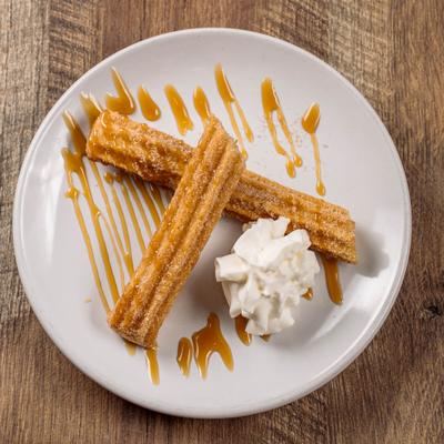 Plate of churros drizzled with caramel sauce, with whipped cream on the side.