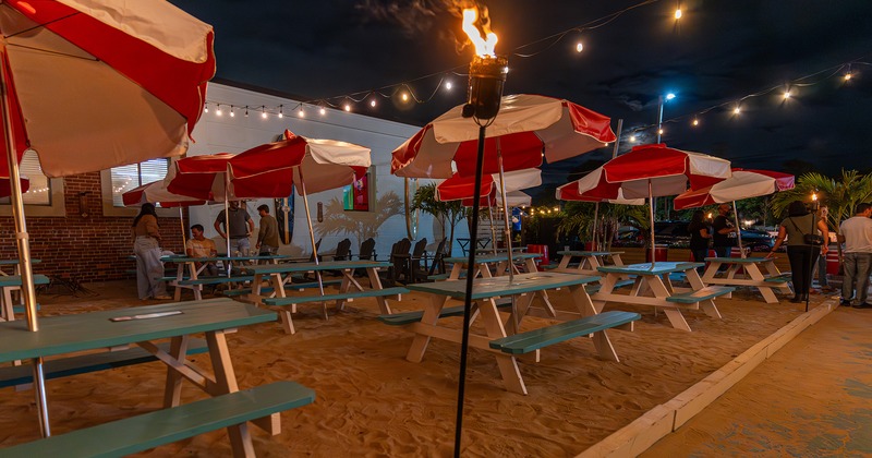 Outdoor seating area at night, wooden tables with benches and parasols on the sand