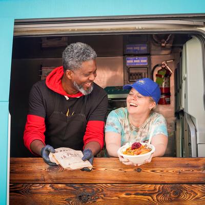 Both owners at the food truck window smiling and holding food.