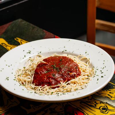 A plate of spaghetti with red sauce and herbs, on a colorful table.