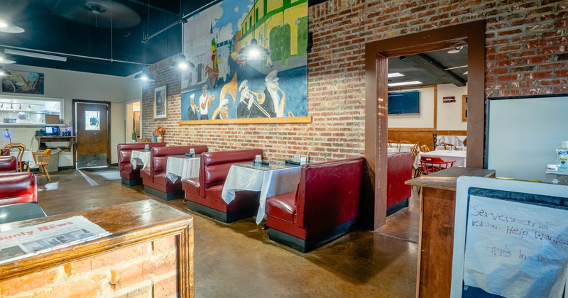 Interior of a brick-walled restaurant with red booths, white tablecloths, hanging lights, and a large jazz-musician mural