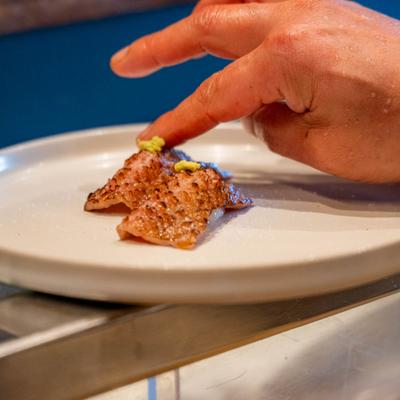 A hand garnishing seared wagyu beef nigiri.