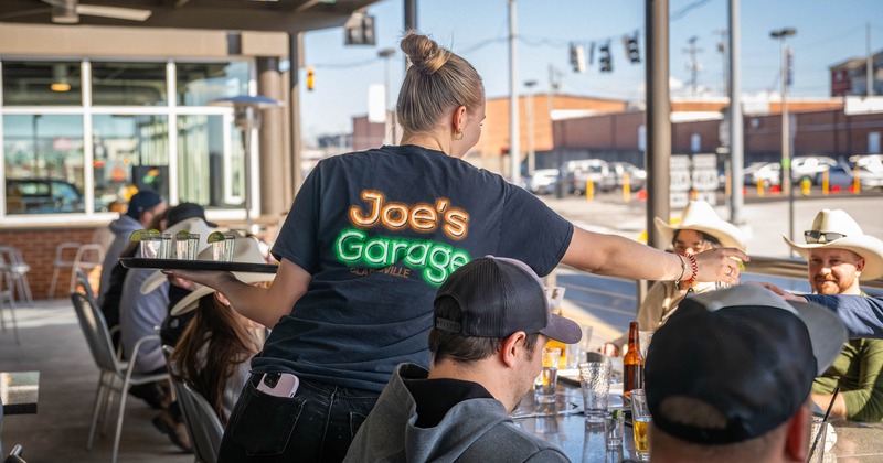 A server hands out shots of tequila to a group of guests sitting outside