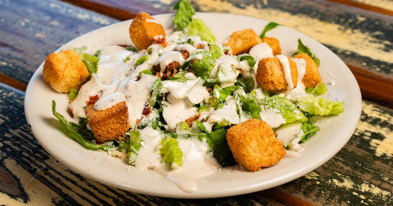 Caesar Salad on a white plate atop a rustic wooden table