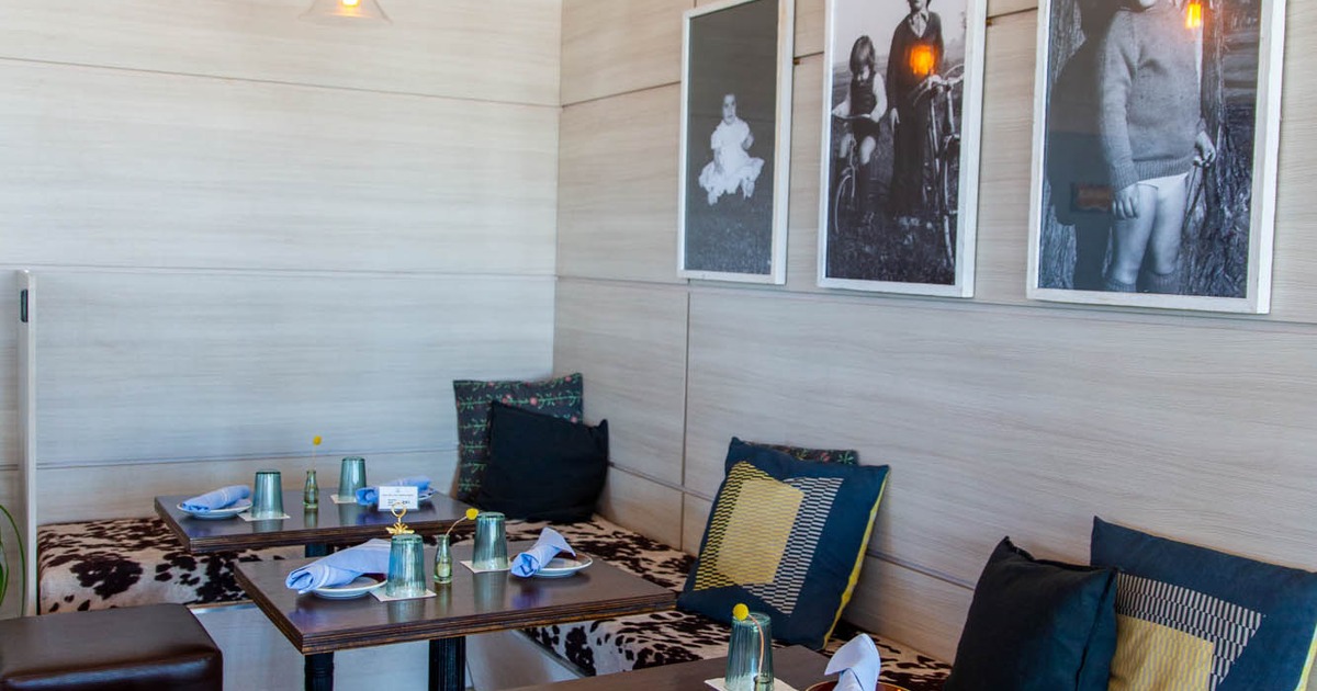 Interior, seating by a wall with pillows and set tables, old photos on the wall