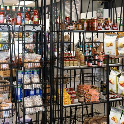 Interior, metal shelves showcasing jars of sauces, preserved foods, and bags of Italian breadsticks.