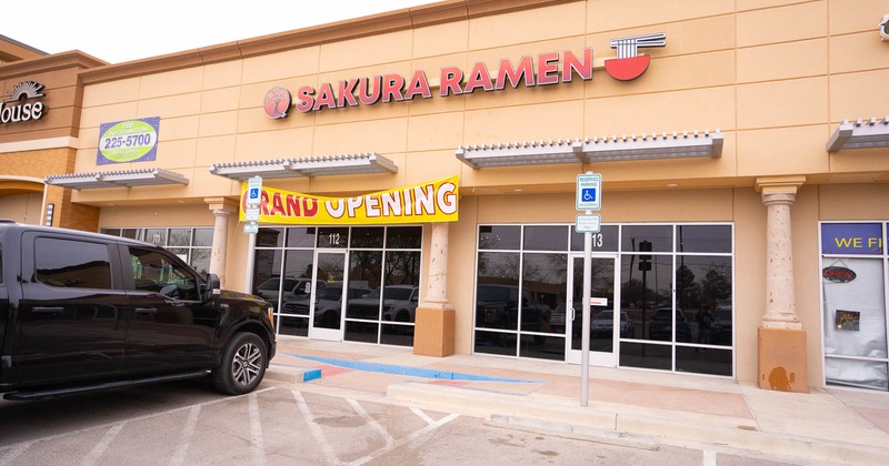 Storefront with signage, grand opening sign, and and a parked car