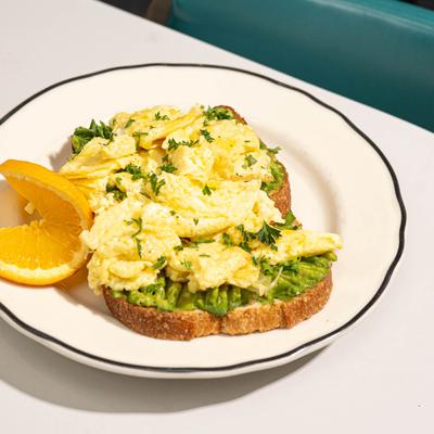 Avocado toast topped with two scrambled eggs, garnished with orange slices.