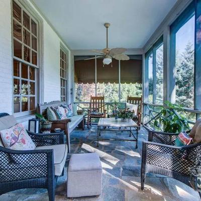 Sunlit screened veranda with wicker chairs, cushioned sofa, coffee table, and stone flooring.