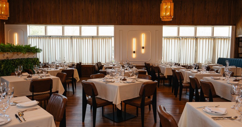 Elegant dining area with tables set, wooden floors and pendant lights.