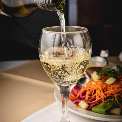 White wine being poured into a glass served alongside a salad.
