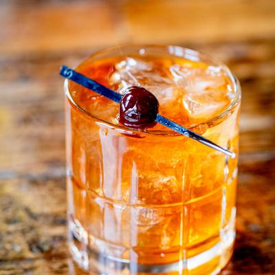 Black barrel old fashioned, garnished with a cherry on a pick.