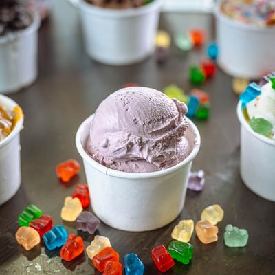 A berry and assorted ice cream cups displayed  on a table with gummy bears.