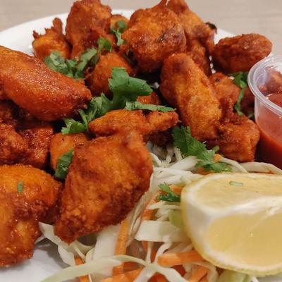 Crispy spiced chicken bites with coleslaw, lemon wedge, and red dipping sauce.