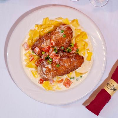 Stuffed and breaded chicken, with creamy sauce, tomatoes, peas, and pasta.
