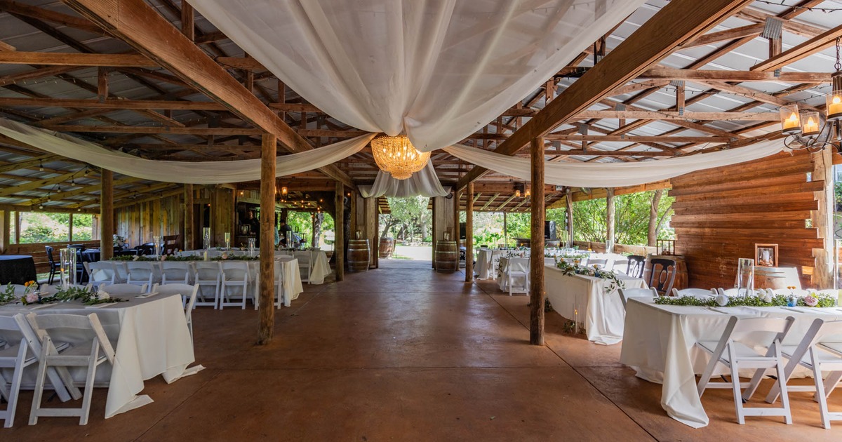 A rustic barn like space set for a wedding reception, with white drapes on the ceiling