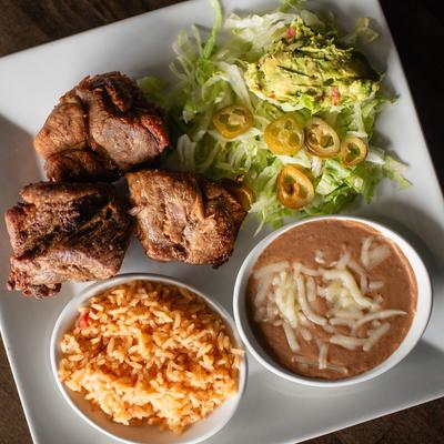 Pork tips served with rice, beans, lettuce, and guacamole.
