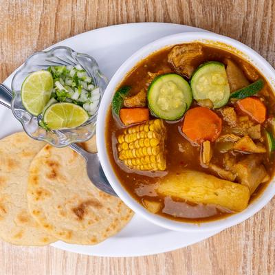 Tripe soup, with carrots, corn, cucumber, with salad and tortillas on the side, topview