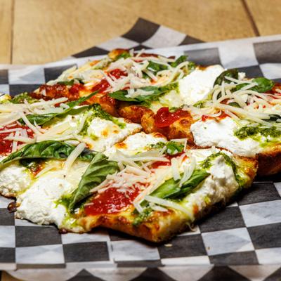 Pesto Pizza on Italian bread served on checkered paper.
