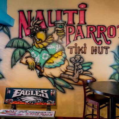 Colorful Nauti Parrot Tiki Hut wall mural with a cartoon parrot and palm trees.