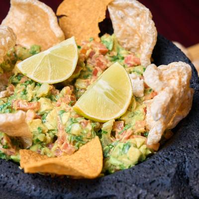 Guacamole served in a traditional stone mortar with lime, chips and pork rinds.