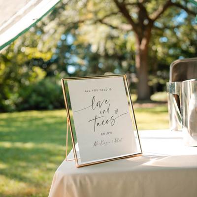 Outdoors, a Taco bar sign on a buffet table.