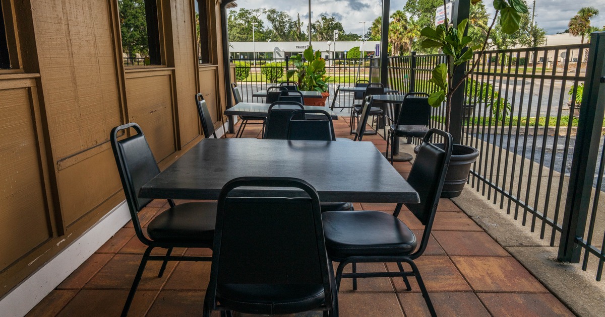 Outdoor patio dining area with tables, chairs and potted plants on a tiled floor