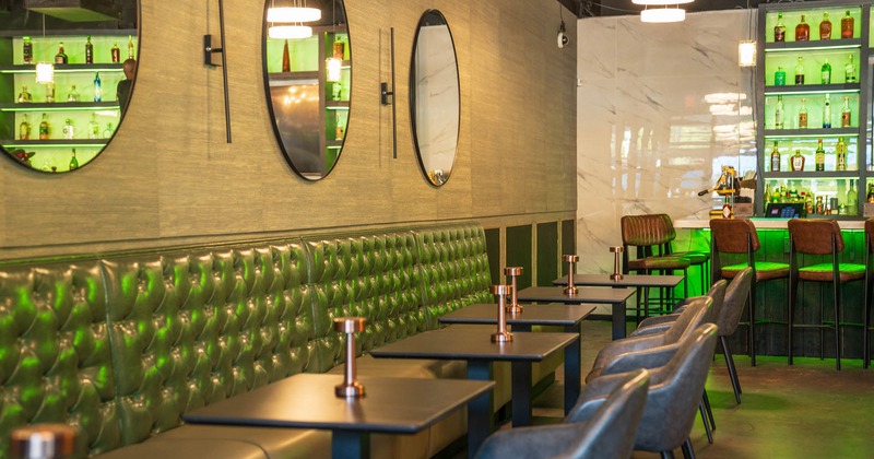 Interior, padded banquette bench with tables and chairs, bar in the back, concrete flooring