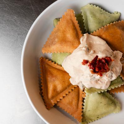 Green and orange ravioli topped with creamy sauce and sun-dried tomatoes.
