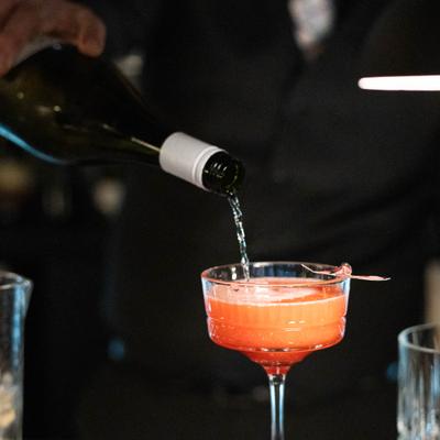 Cocktail in coupette glass being toped up with sparkling vine.