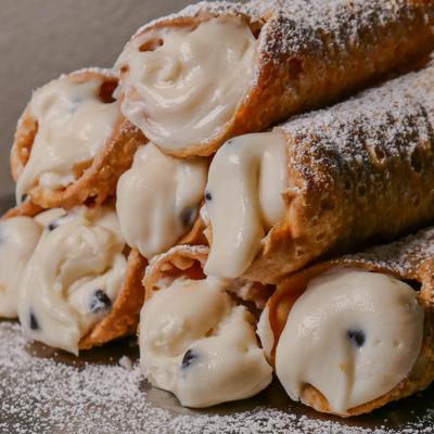 Stacked mini cannoli filled with cream and chocolate chips, dusted with powdered sugar.