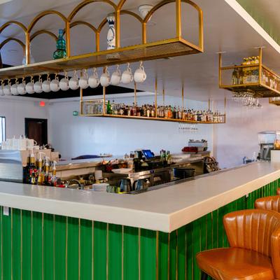 Bar area with a counter, orange tufted bar stools and custom ceiling shelving.
