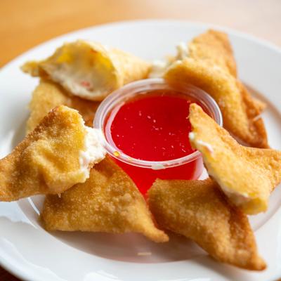 Crab Rangoon served with a side of bright red dipping sauce.