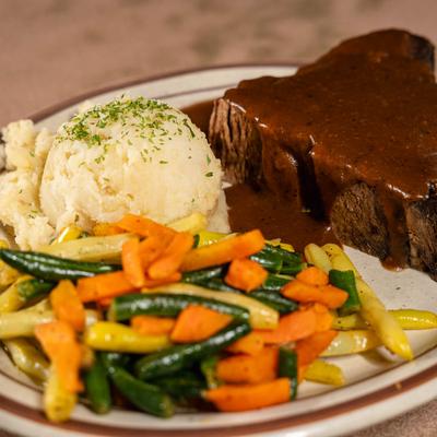 Pot roast covered in gravy, with mashed potatoes, green beans, and carrots.