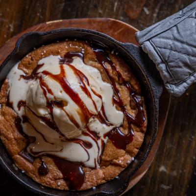 Skillet cookie topped with vanilla ice cream and chocolate syrup.