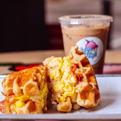 Waffle breakfast sandwich with iced coffee behind it.