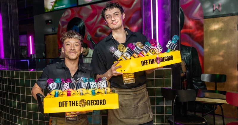 Staff members holding trays of colorful, decorated microphone-shaped props