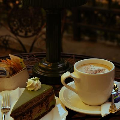 Cappuccino with a layered cake slice on an outdoor table.