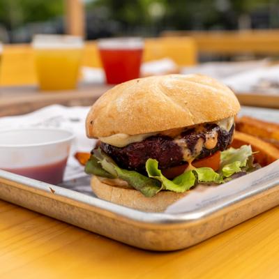 Smoked burger served on a metal tray with a side of sauce and French fries.