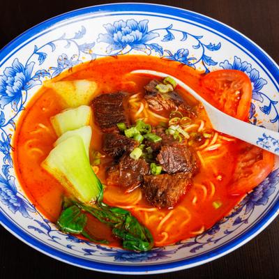 Spicy beef noodle soup with bok choy, tomatoes, and scallions.