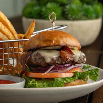 Bacon cheeseburger with lettuce, tomatoes, and onions, served with fries and ketchup.