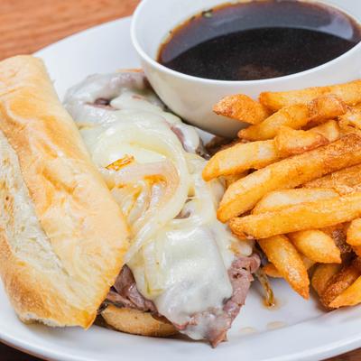 Close up of French dip sandwich with beef broth and fries.
