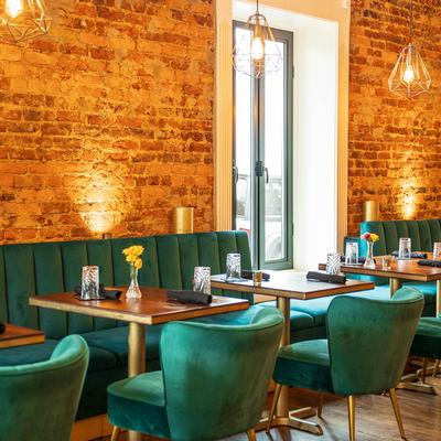 Interior with exposed brick walls, green velvet seating, and pendant lights.