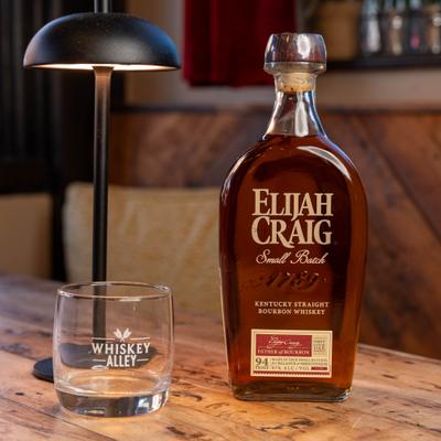 Whiskey bottle and a glass on a table beside a lamp.